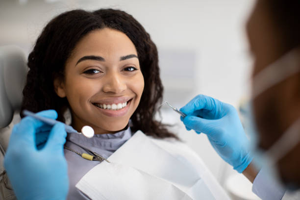 Portrait Of Smiling Black Female Patient Having Dental Treatment With Stomatologist Man, Happy African American Woman Sitting At Dentist Chair In Modern Clinic And Looking At Camera, Closeup